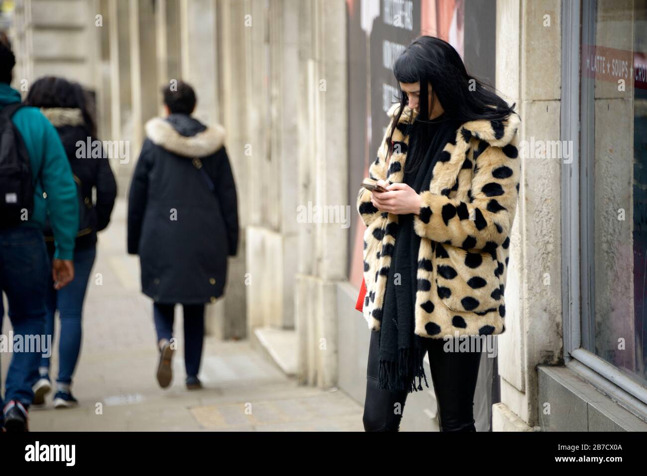 Young woman in animal print fur coat, checking her phone Stock Photo
