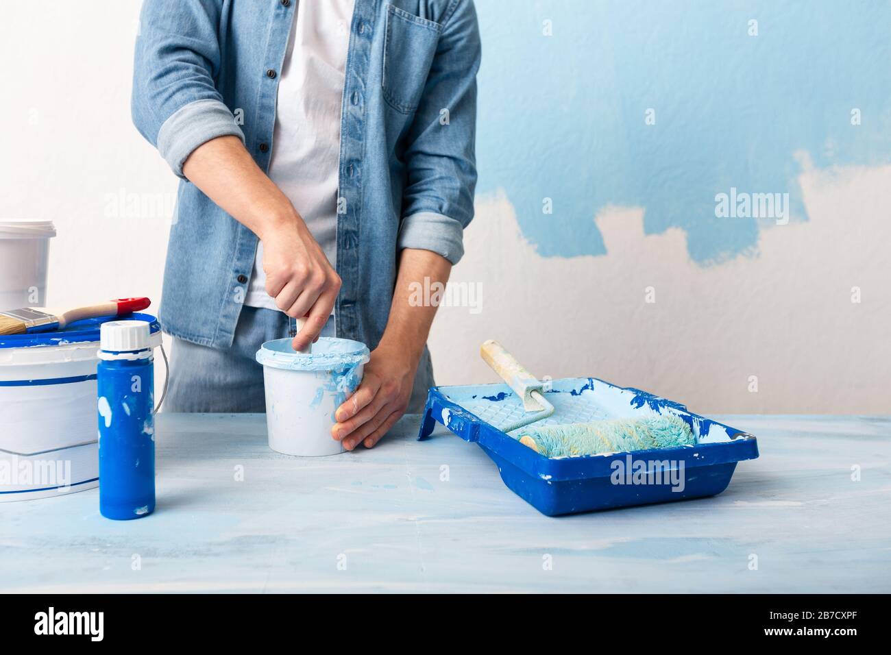 Man in jeans mixes paint in bucket Stock Photo