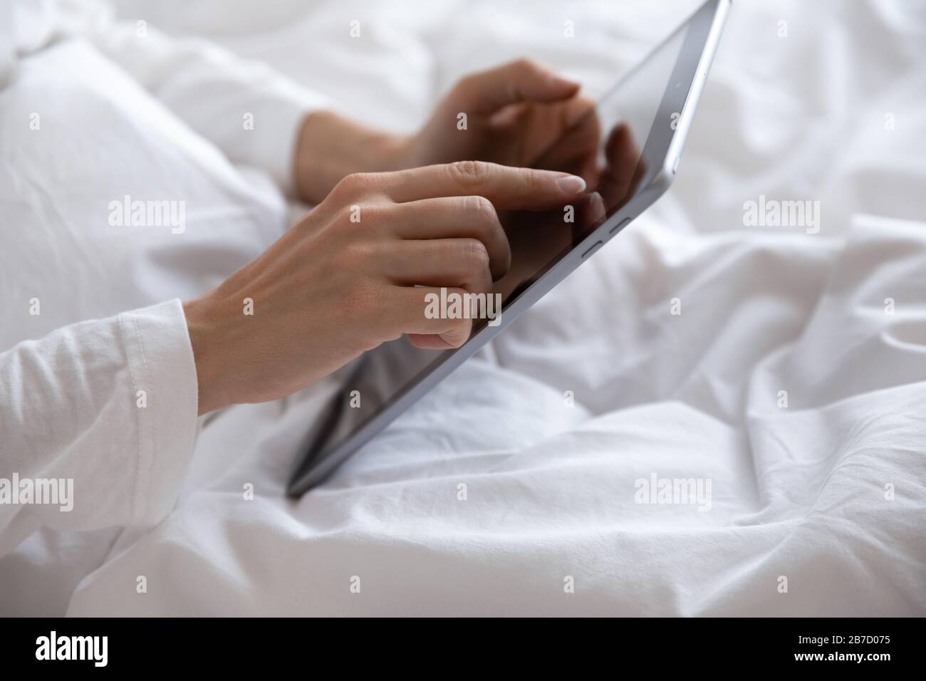 Young woman lying in bed, using computer digital tablet. Stock Photo