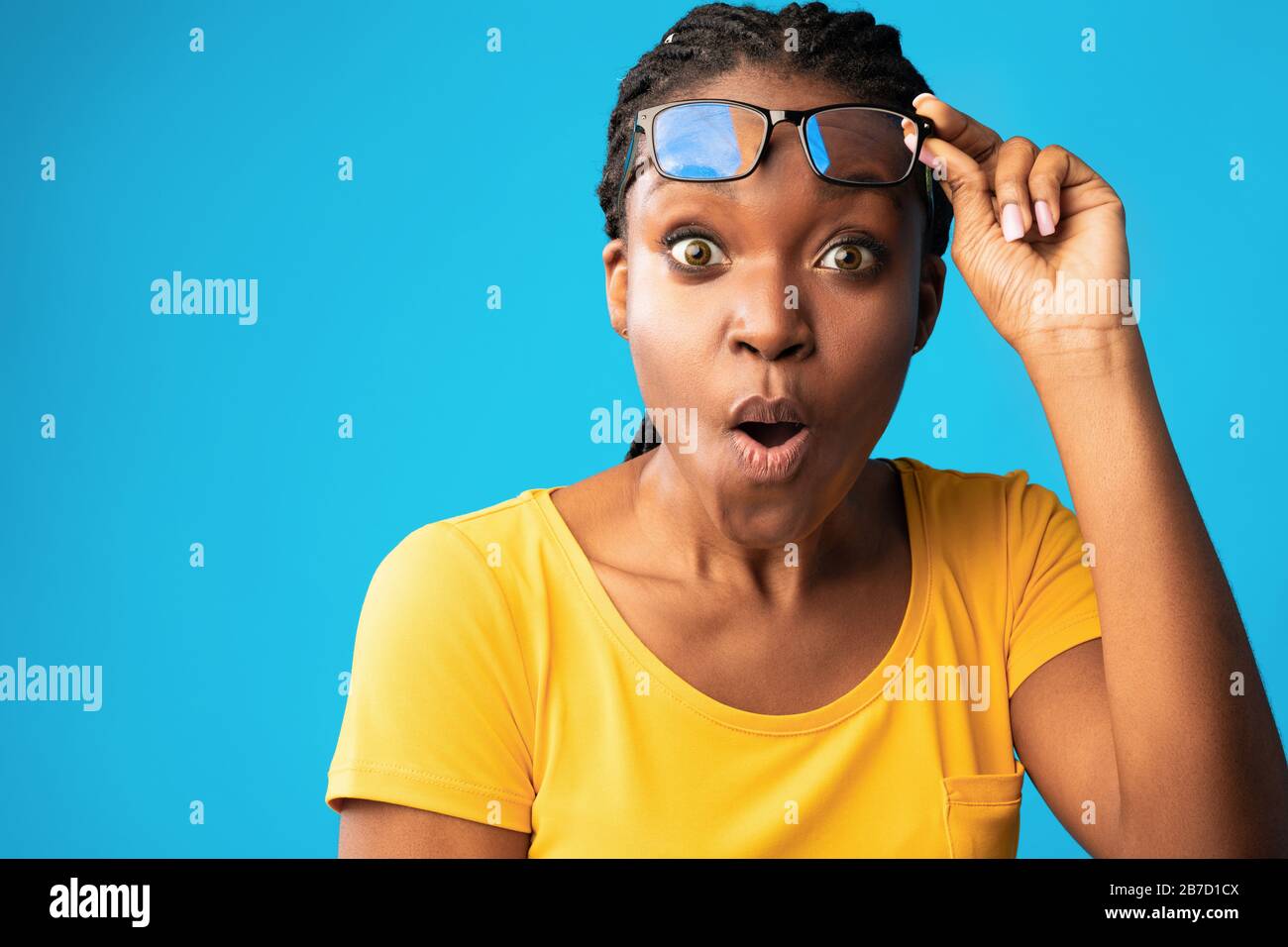 Shocked African Woman Looking At Camera Rising Eyeglasses, Blue Background Stock Photo