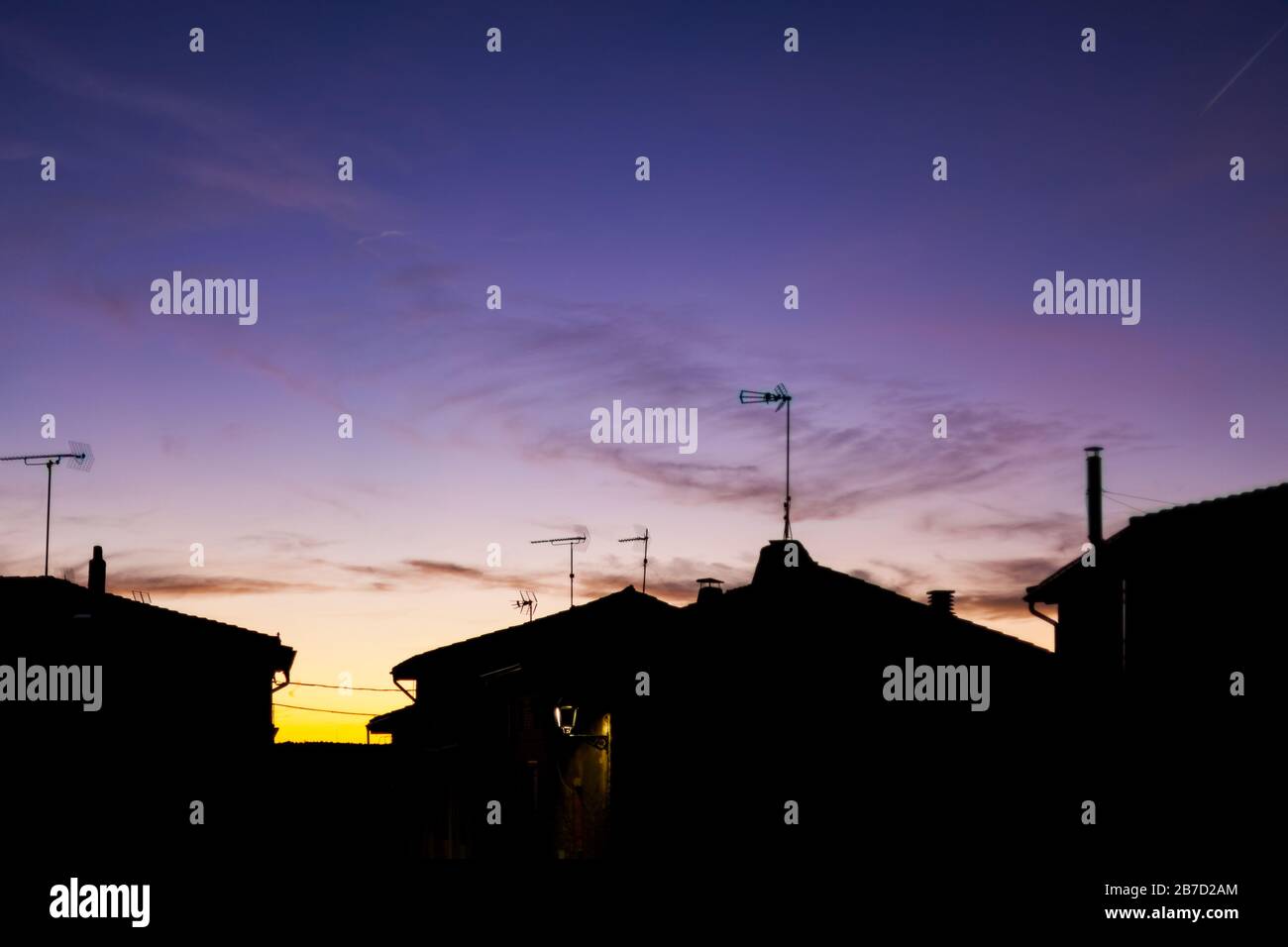 Sunset in the village with silhouettes of antennas and chimneys with purple sky Stock Photo