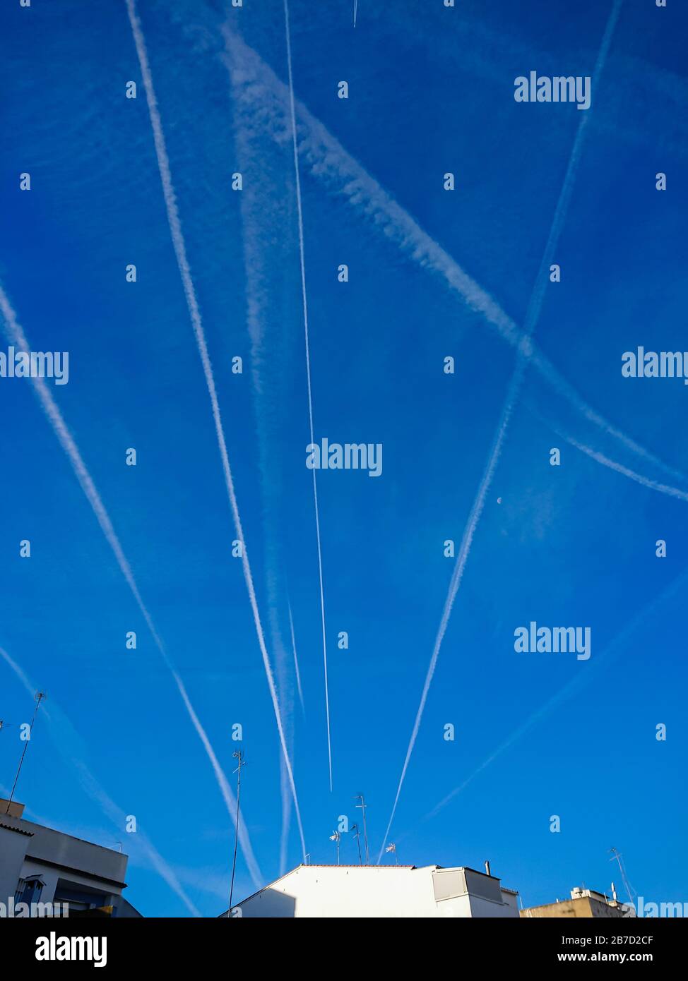 Airplane chemtrails over the city in blue sky with clouds Stock Photo