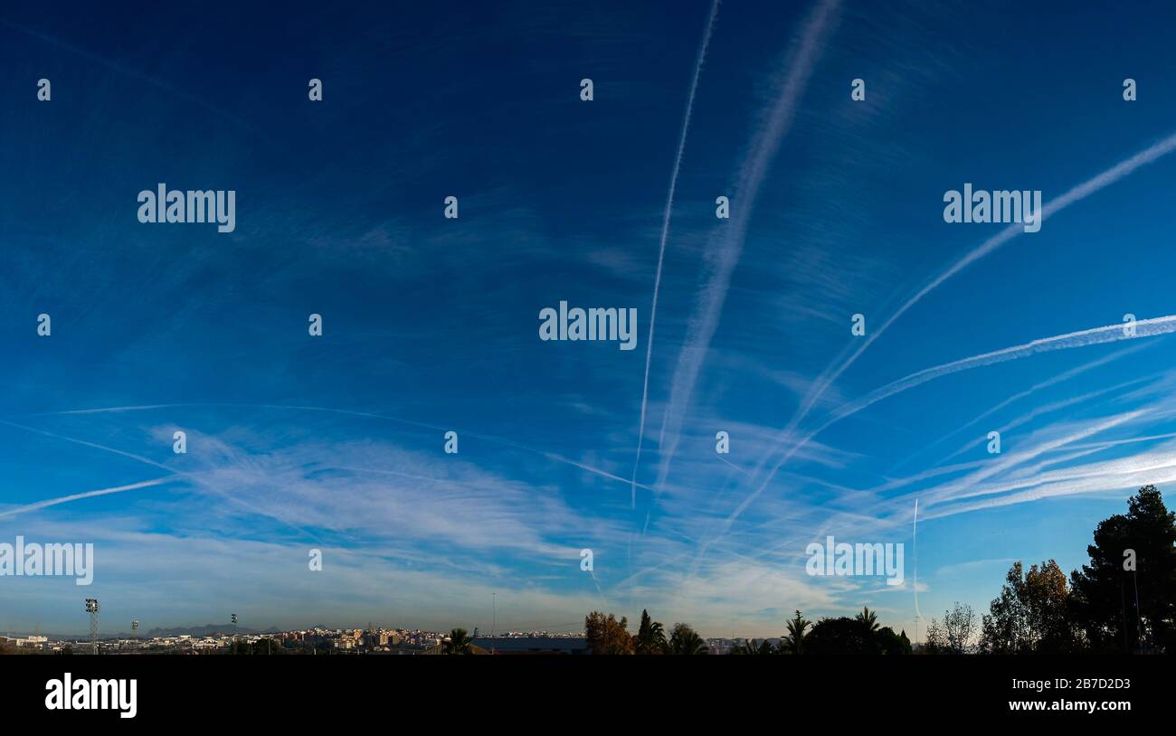 Airplane chemtrails over the trees in blue sky with clouds Stock Photo