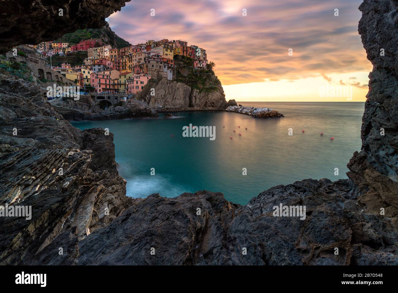 Cloudy sky at sunrise on Manarola framed by rocks, Cinque Terre, La Spezia province, Liguria, Italy Stock Photo