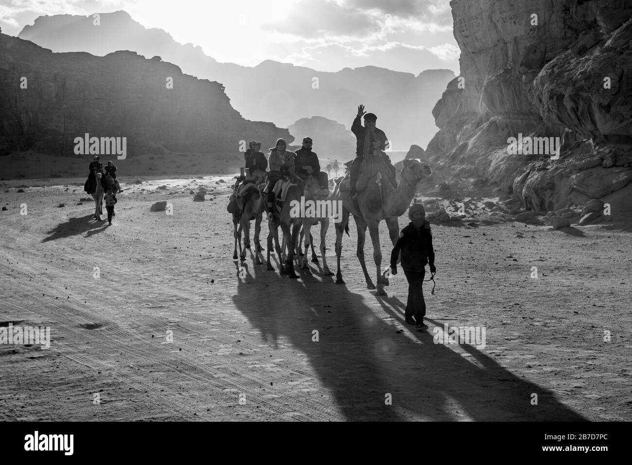 WADI RUM, JORDAN - JANUARY 31, 2020: Impressive sky with sun rays over people riding camels. Black and white image, winter puffy clouds afternoon sky. Desert, Hashemite Kingdom of Jordan Stock Photo