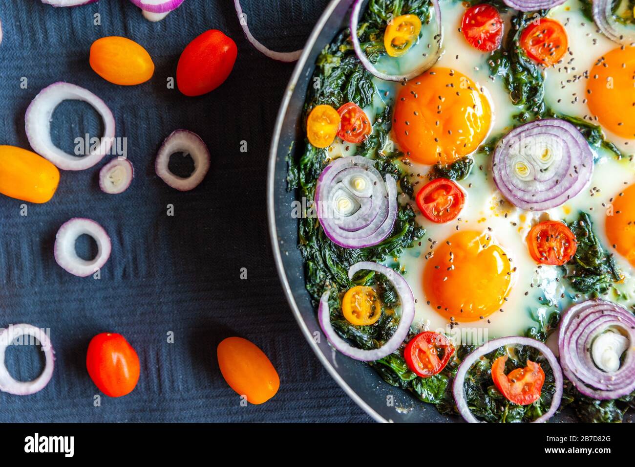 Close up shot of a omelette with spinach in a pan and decorated with fresh onion, tomatoes and spinach Stock Photo
