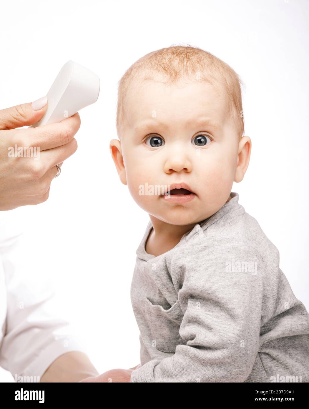 Pediatrician or nurse checks baby girl's body temperature using infrared forehead thermometer