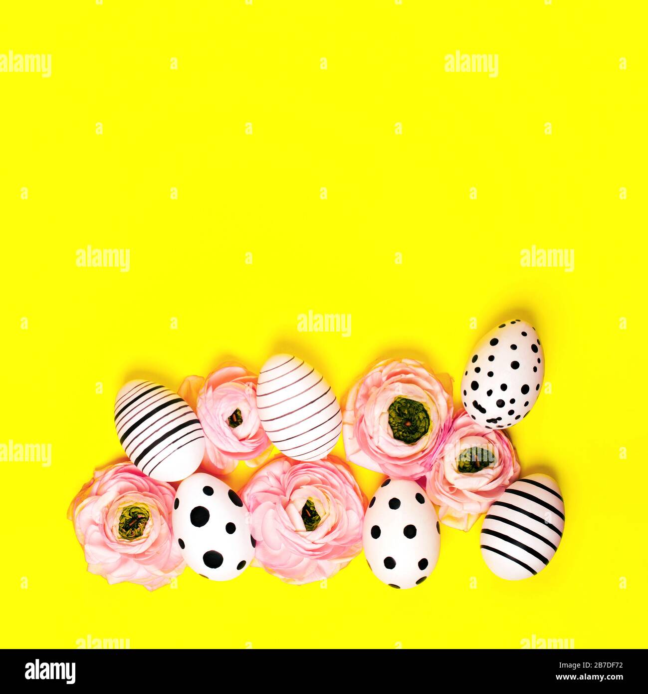 Creative graphic hand-painted eggs and ranunculus flowers on bright yellow background. Easter concept. Stock Photo