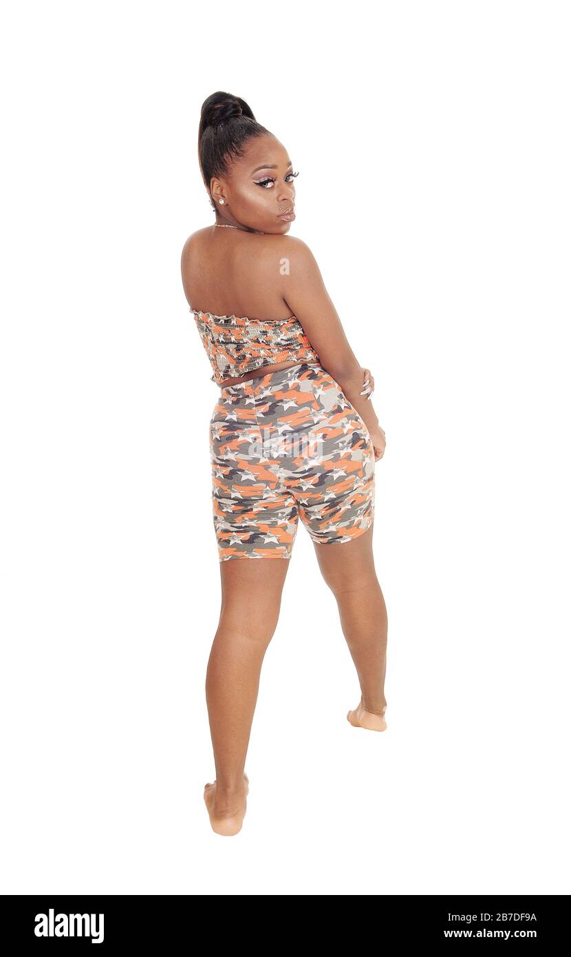 A lovely young African woman standing in a beach outfit in the studio from the back, looking over her shoulder, isolated for white background Stock Photo