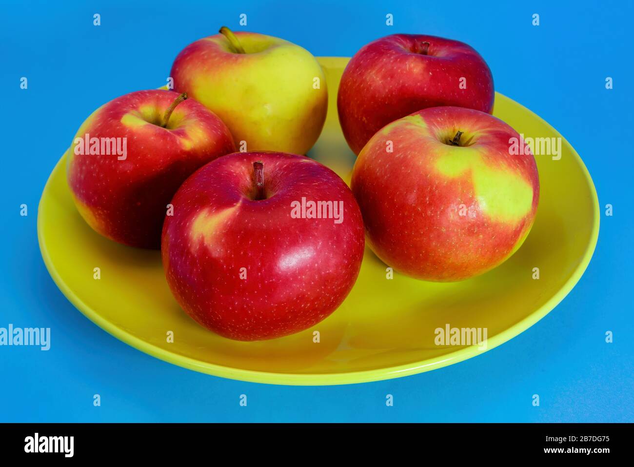 Four fresh wet red apples isolated on blue background. Stock Photo