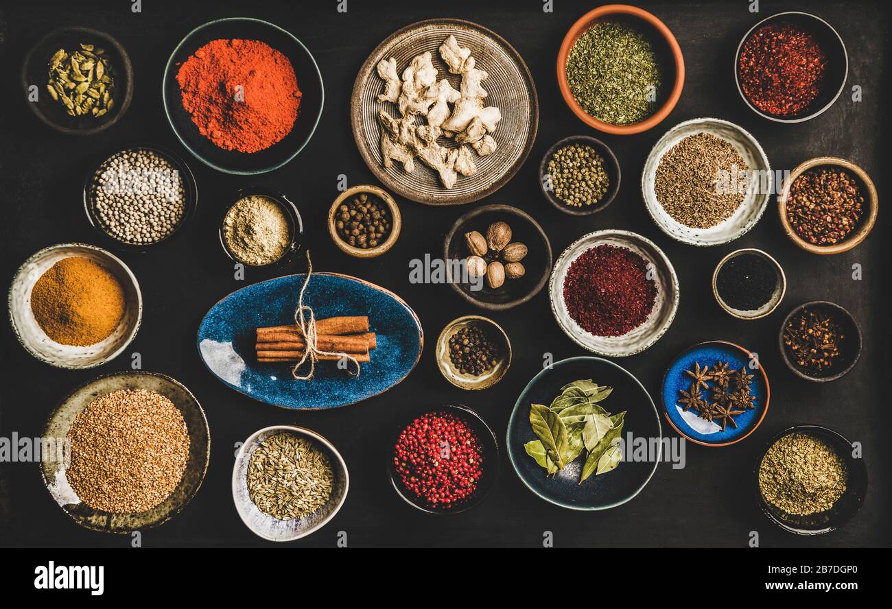 Flatlay of spices in bowls and plates over dark background, top view