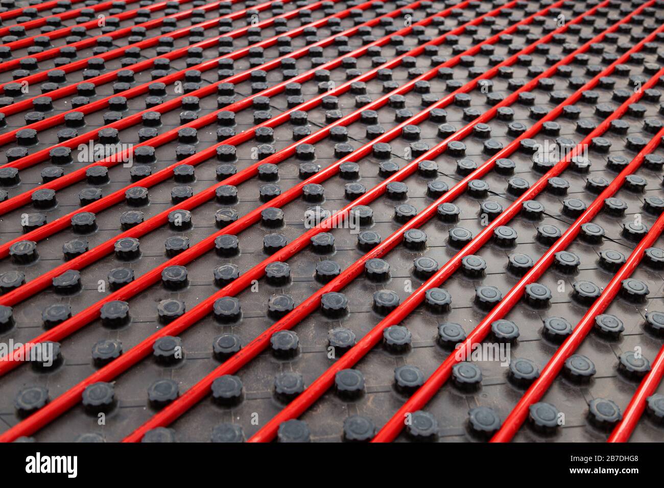 Radiant underfloor heating installation with red flexible tubing mounted on black insulation boards Stock Photo