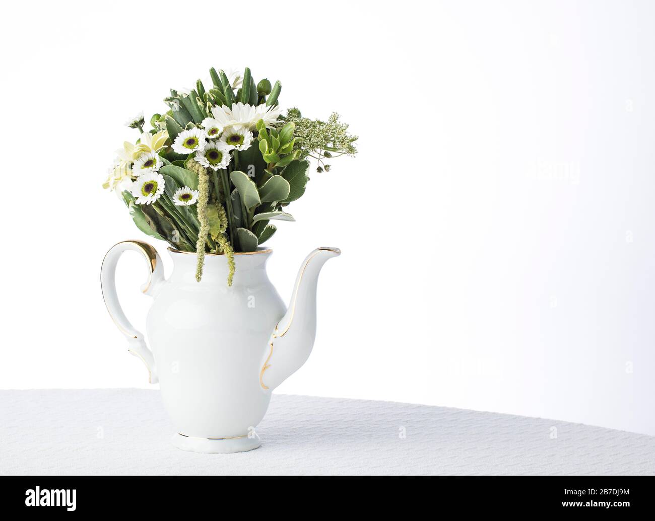 White tablecloth and white china set off the greenery and white flower petals in the floral centerpiece Stock Photo