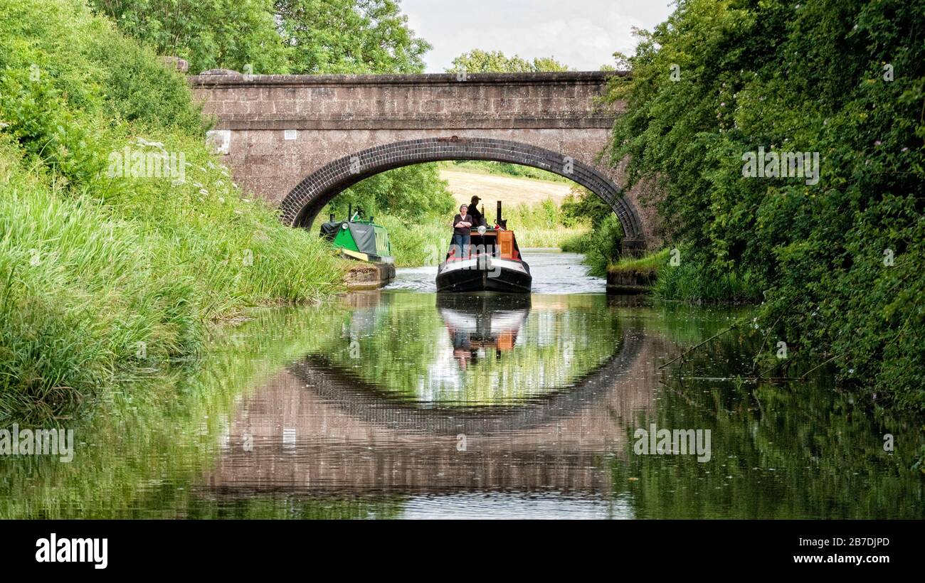 Narrowboat cruising under an arched road bridge on the Grand Union Canal Leicester Arm,  England, UK, Britain, Leicestershire Stock Photo