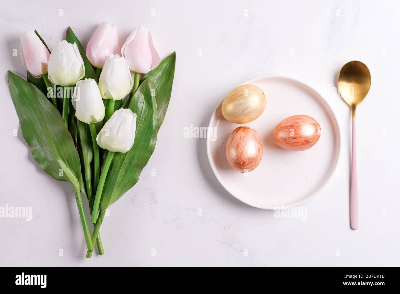 Easter plate with spring tulips and spoon and golden eggs on stone Stock Photo