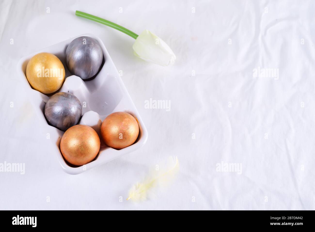 Golden Easter Eggs in ceramic egg tray with tulip on white table. Easter background or easter concept. Stock Photo