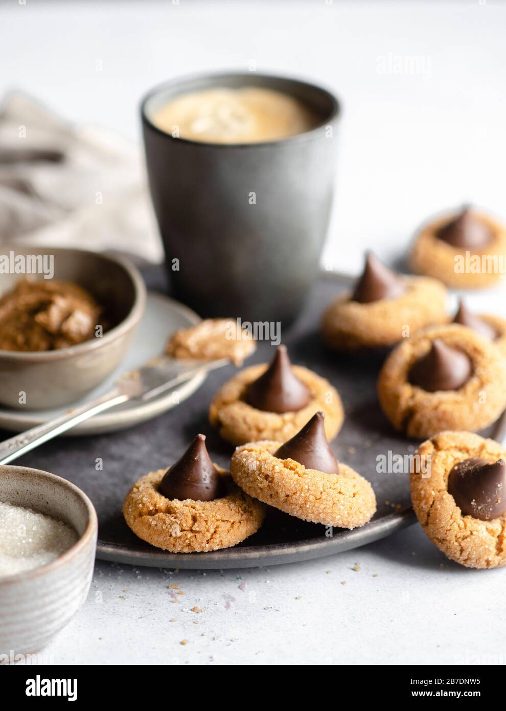 Peanut butter in a pinch bowl on a dark grey plate surrounded by chocolate kisses cookies Stock Photo