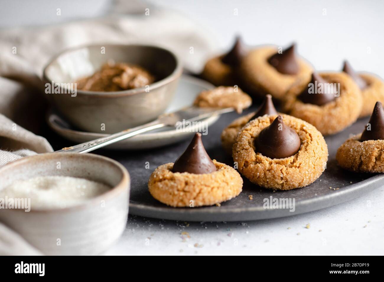 Peanut butter in a pinch bowl on a dark grey plate surrounded by chocolate kisses cookies Stock Photo