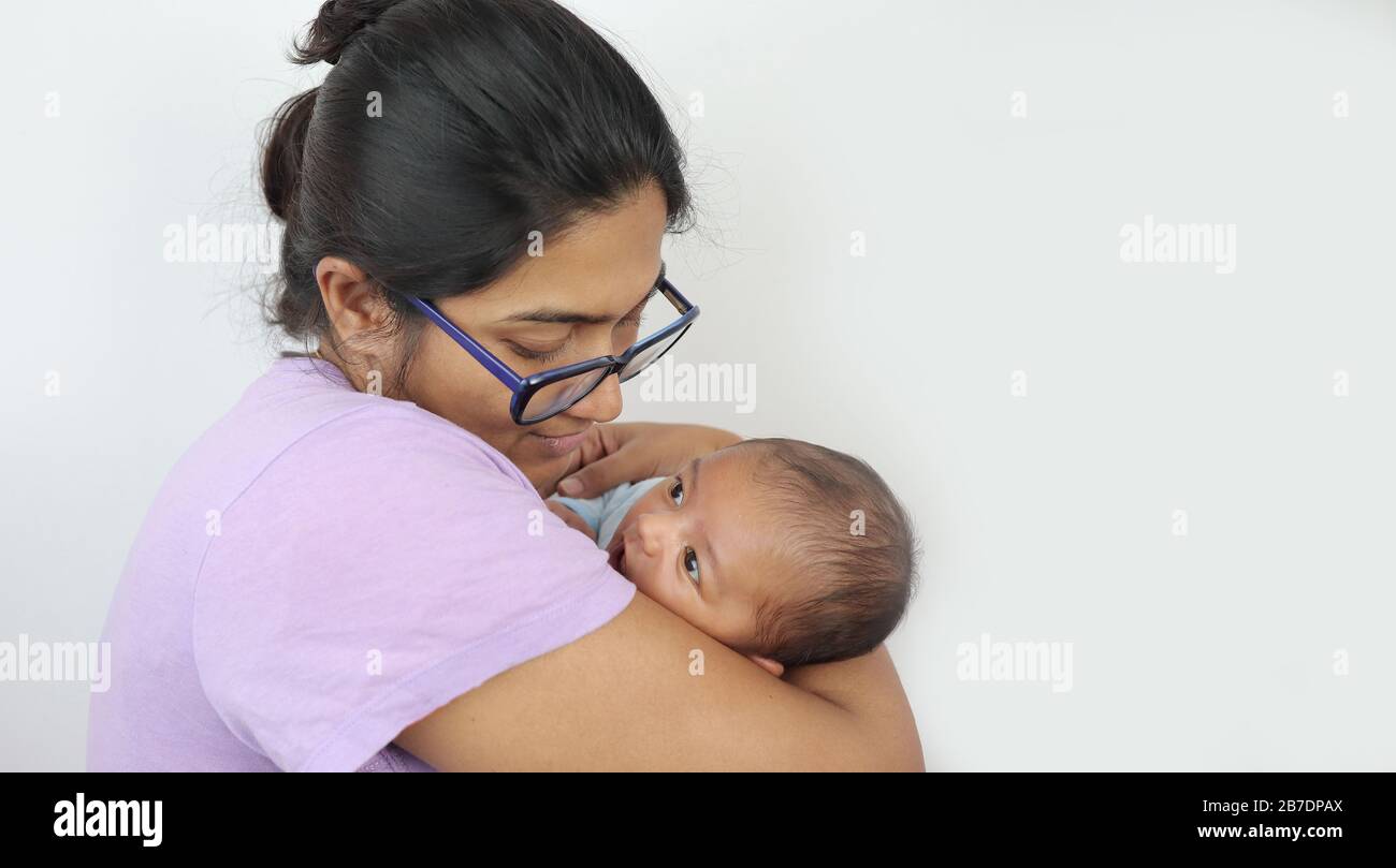a young mother in spectacles looking at her infant baby boy in her lap in solid grey background with space for text. mothers day concept photo. Stock Photo