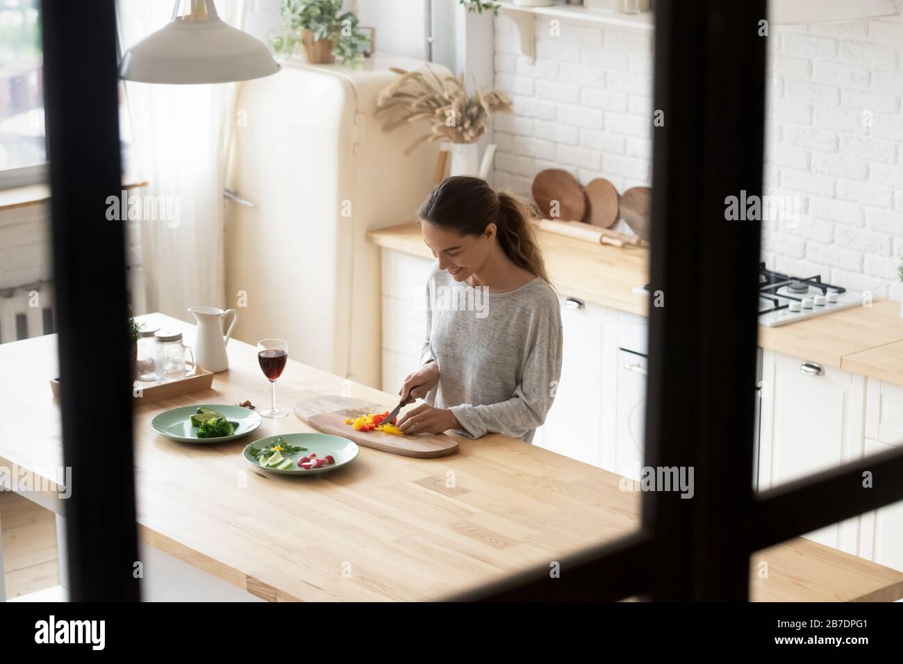 Smiling young woman cutting vegetables, cooking salad in kitchen Stock Photo