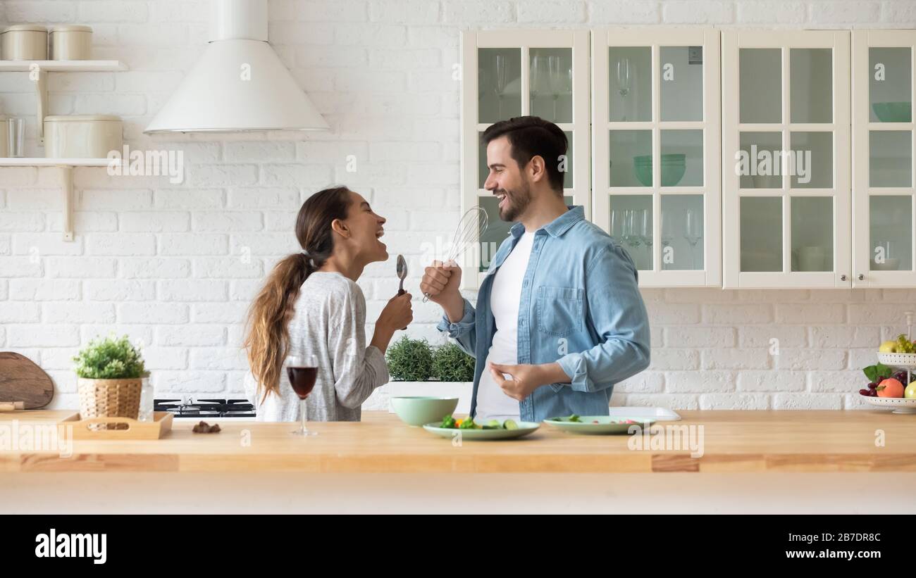 Happy loving couple singing, having fun with kitchenware in kitchen Stock Photo