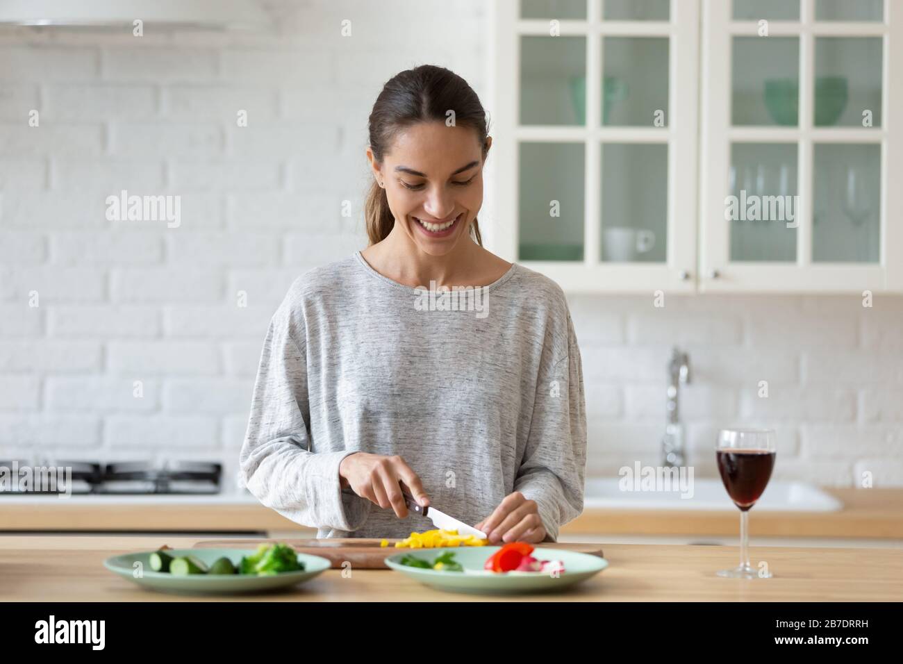 Smiling young woman cutting vegetables for salad in kitchen Stock Photo