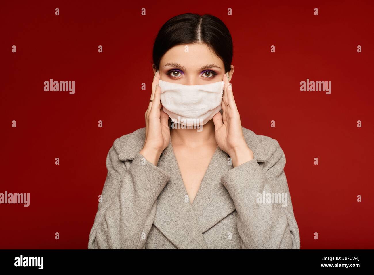 Portrait of a young woman in a protective face mask isolated at the red ...