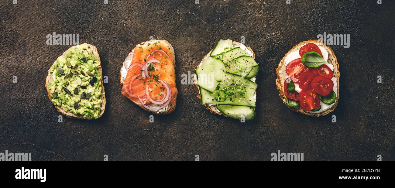 Variety of sandwiches for breakfast, snack, appetizers - avocado puree, mozzarella, tomatoes, basil, cream cheese, smoked salmon, red onion, cucumber Stock Photo