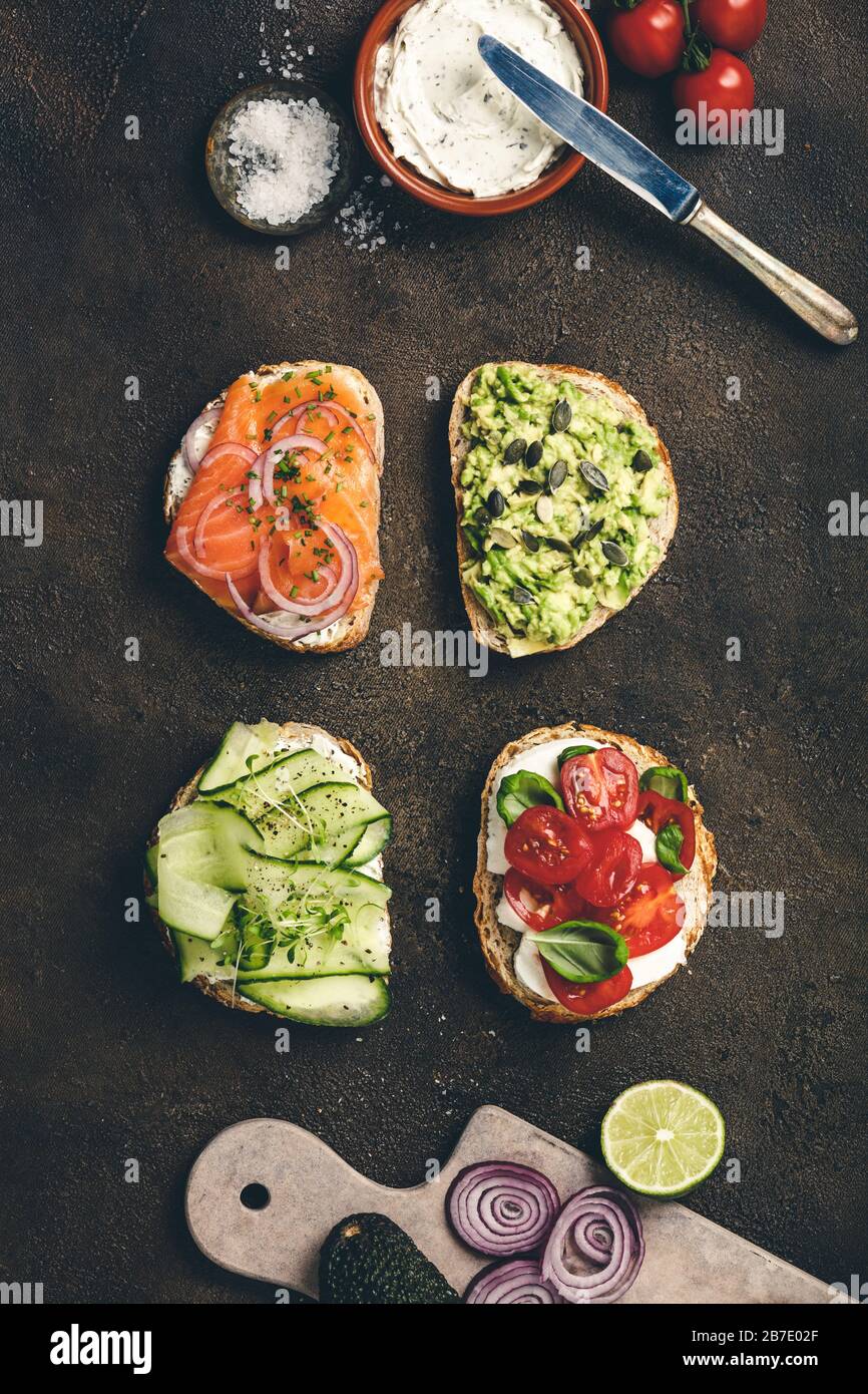 Variety of sandwiches and ingredients. Avocado puree, mozzarella, tomatoes, basil, cream cheese, smoked salmon, red onion, cucumber whole grain bread Stock Photo