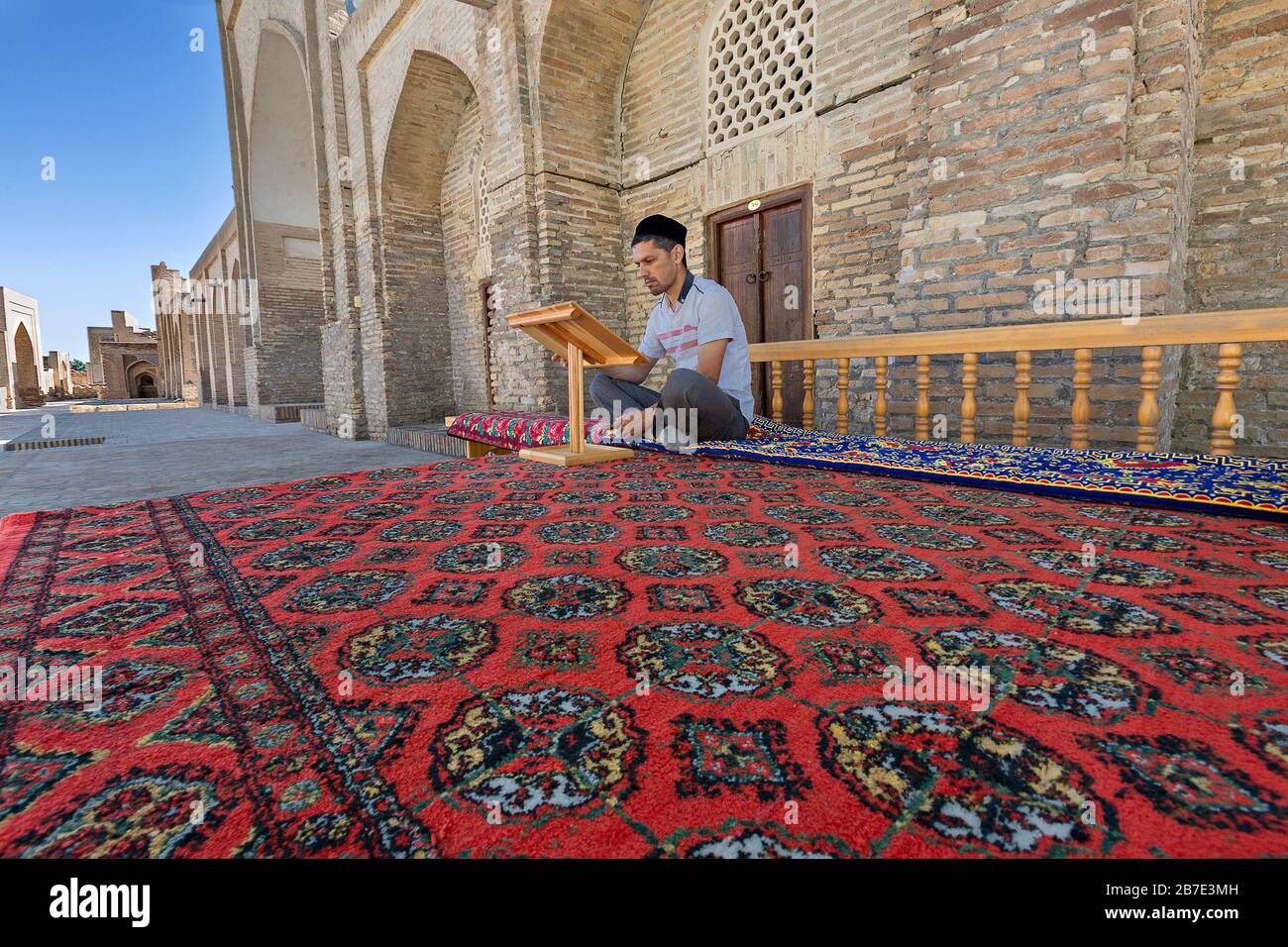Uzbek man sitting on the carpet and reading in the courtyard of Chor Bakr religious complex, in Bukhara, Uzbekistan Stock Photo