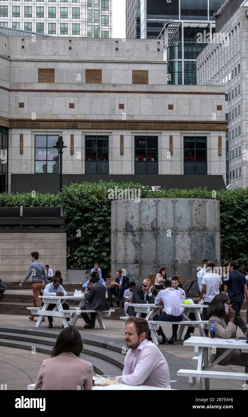 London office workers eat lunch, chat & socialise at outside tables at Cabot Square, Canary Wharf, on a warm day. Tall office buildings in background. Stock Photo