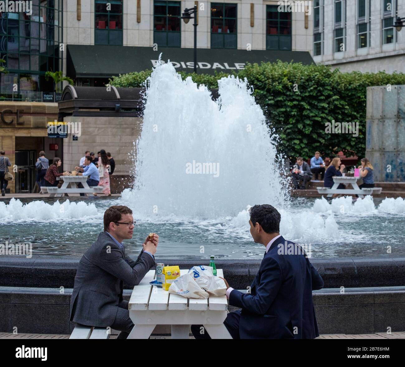 Two men in suits each and chat at outside table next to water fountain  during lunchtime at Cabot Square, Canary Wharf, London, on a warm day Stock  Photo - Alamy