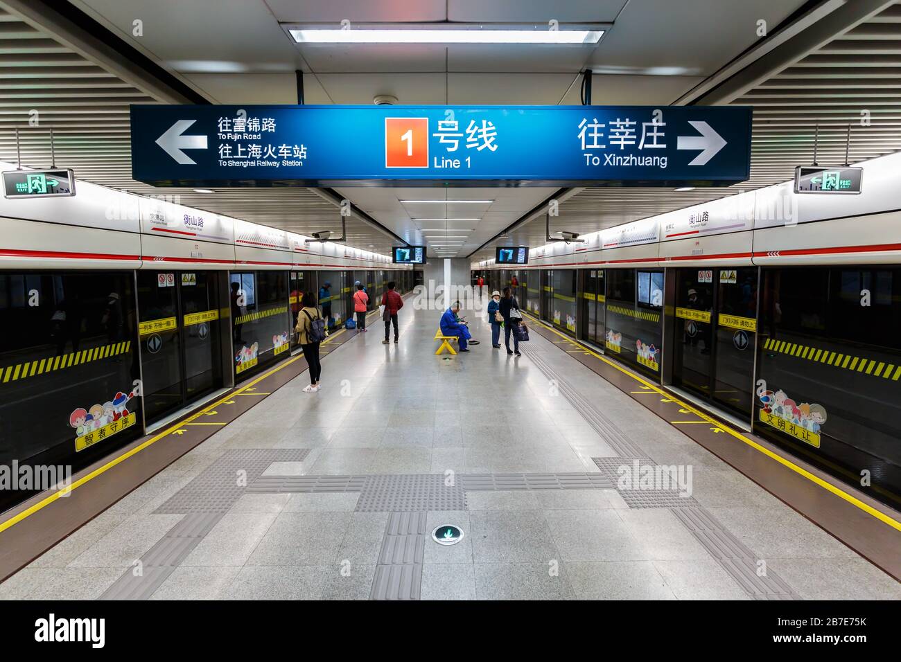 Interior view at the platform of Hengshan Road metro station. A sign is indicating the directions of both tracks. With waiting passengers. Stock Photo
