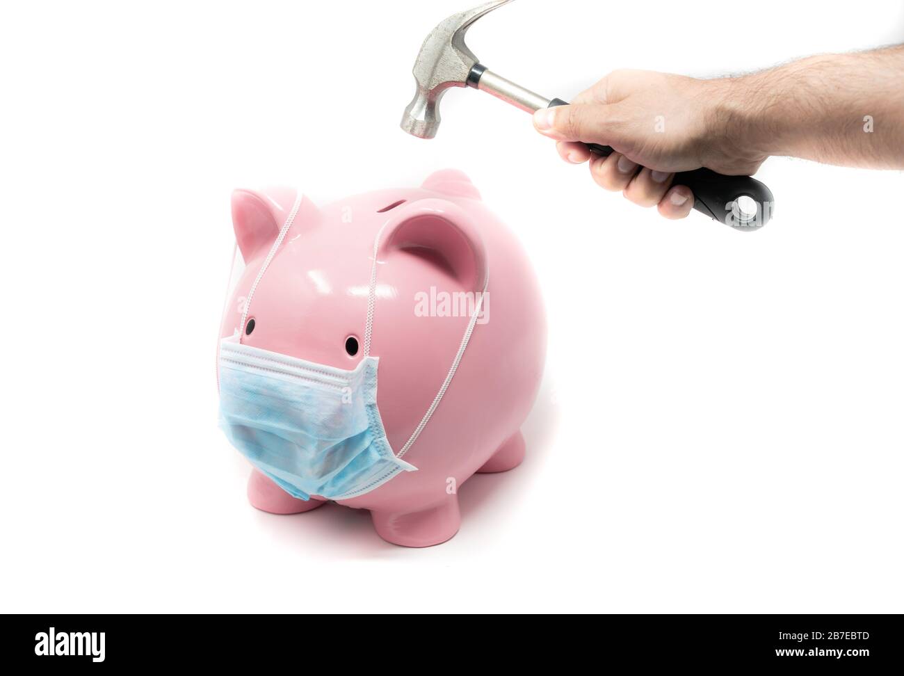 Piggybank wearing surgery mask and hand with hummer ready to crash it. Concept of the impact of a pandemia in world Economy Stock Photo