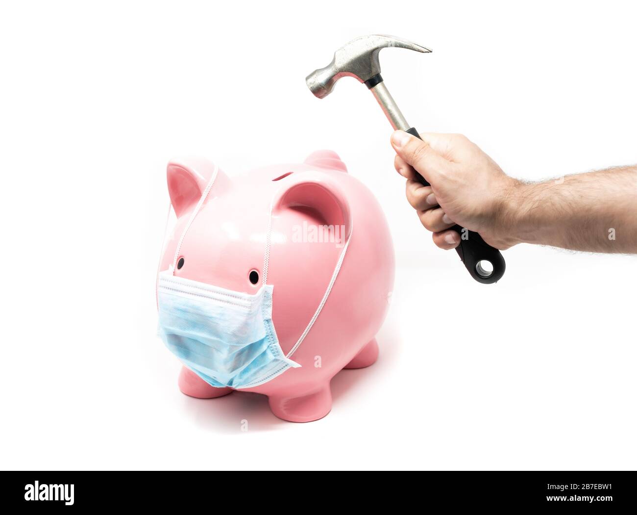 Piggybank wearing surgery mask and hand with hummer ready to crash it. Concept of the impact of a pandemia in world Economy Stock Photo