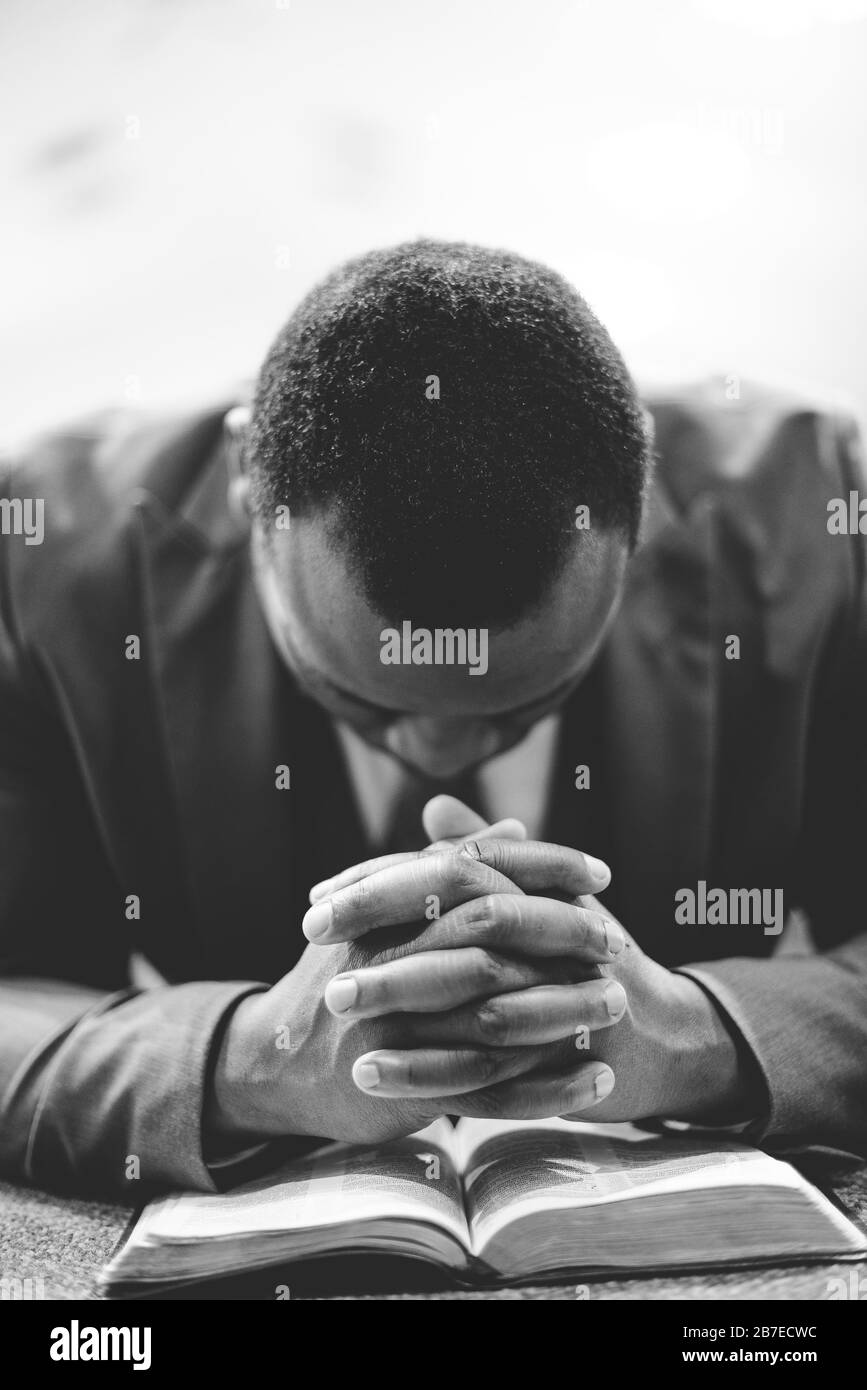 A lonely africanamerican male praying with his hands on the Bible with