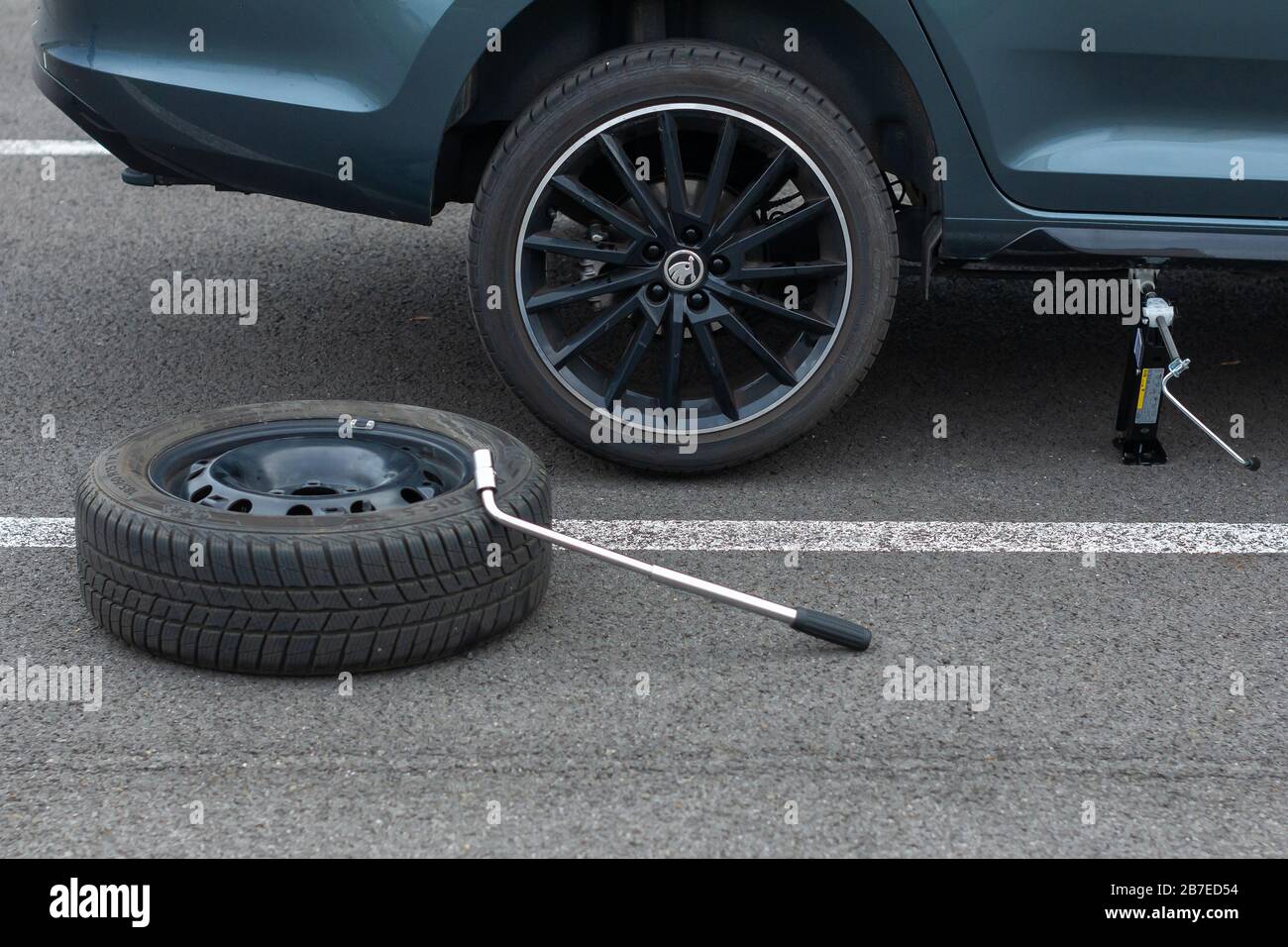 Top view on a flat tire car wheel and screwdriver are on a asphalt road on the broken car background. Jack is lifting up a vehicle. Automobile service Stock Photo