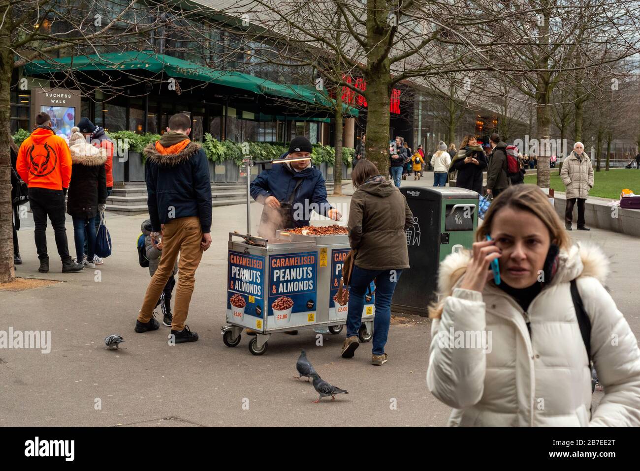 People buying caramelised peanuts and almonds from street food vendor with heated mobile stall at the South Bank Queen's Walk in London, UK as of 2020 Stock Photo