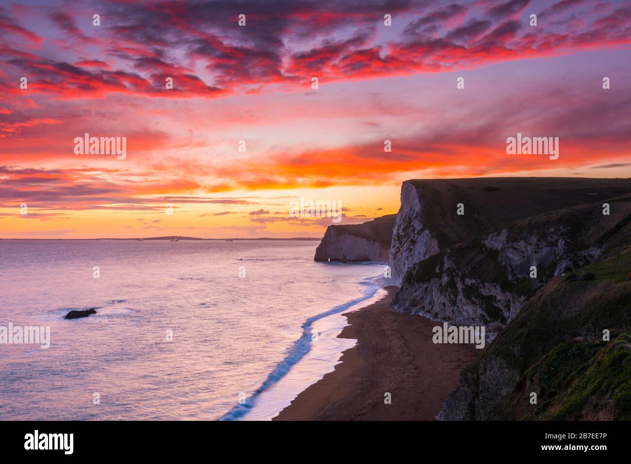 Durdle Door, Lulworth, Dorset, UK.  15th March 2020.  UK Weather.  A spectacular fiery sunset at Durdle Door on the Dorset Jurassic Coast near Lulworth looking towards Swyre Head and Bats Head as the cloud clears as high pressure builds in from the South West.  Picture Credit: Graham Hunt/Alamy Live News Stock Photo
