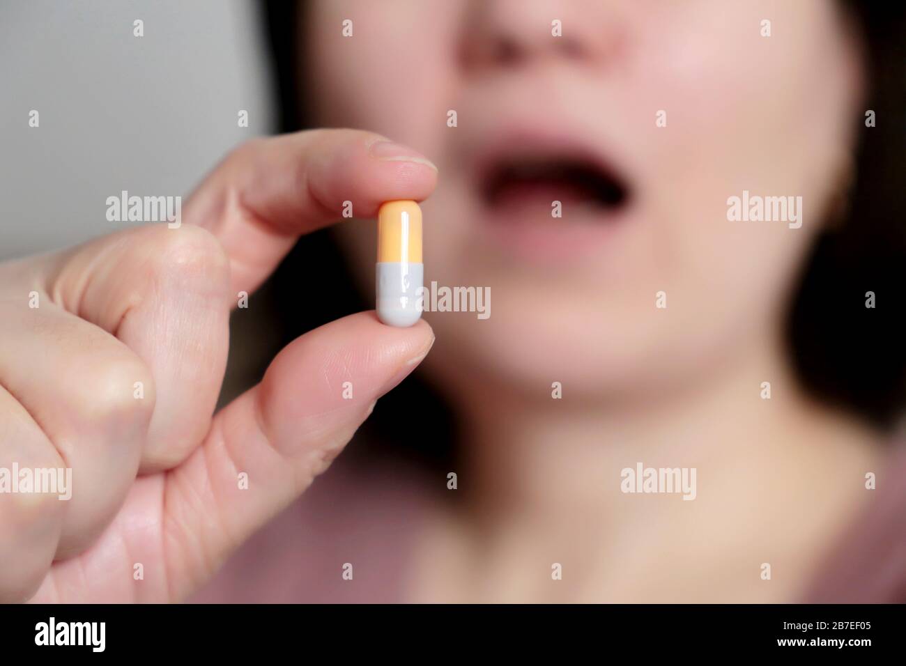 Woman takes a pill, girl putting capsule in open mouth. Sick female taking medicines, concept of antibiotic, vitamin, coronavirus prevention Stock Photo