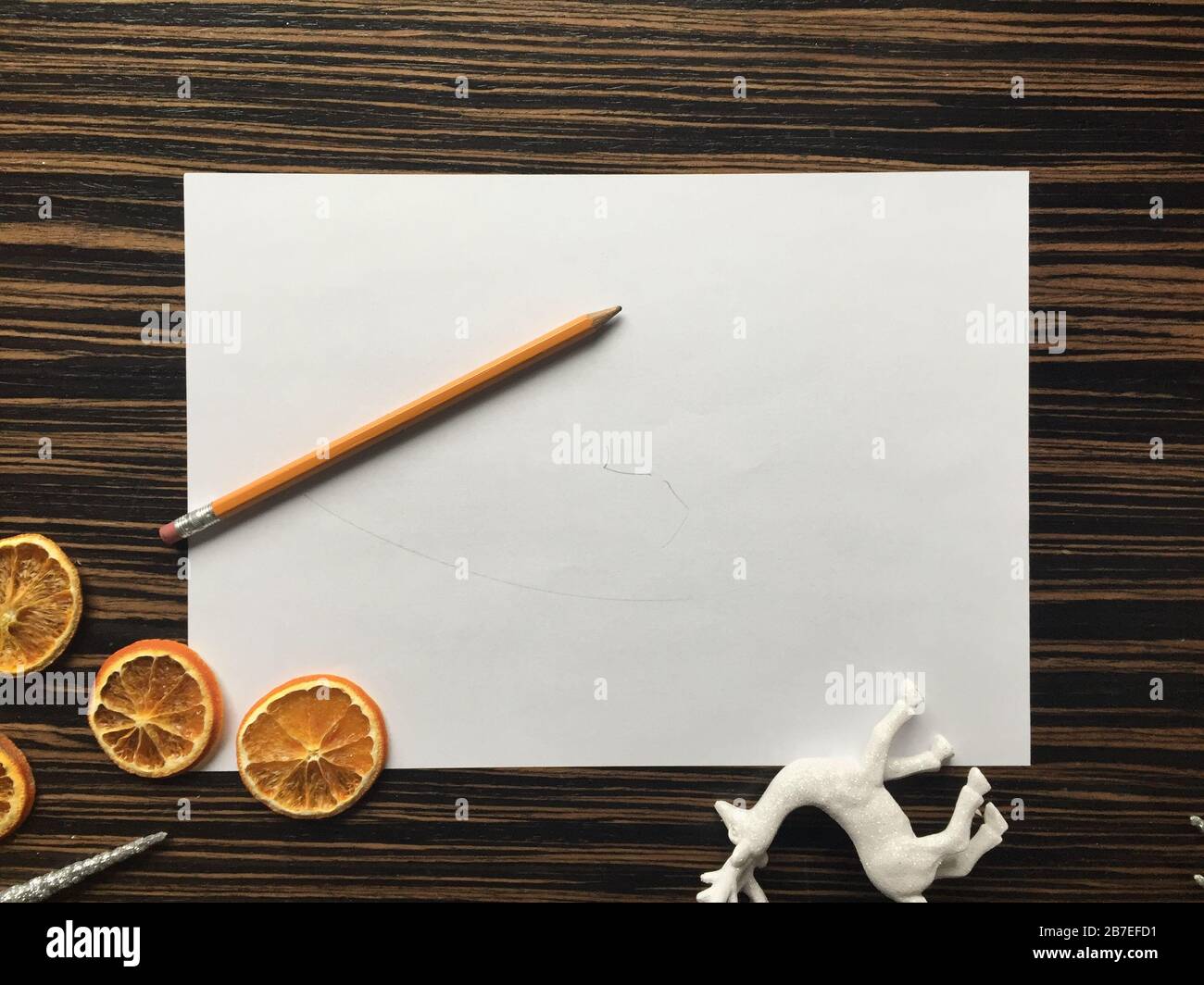White paper put on a wooden surface together with a pencil, oranges and a deer toy Stock Photo
