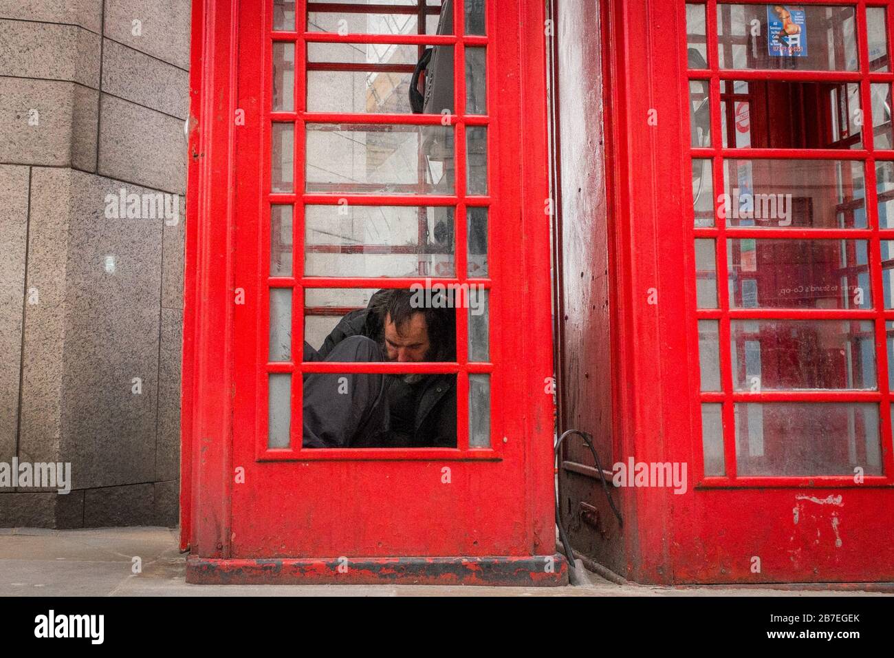 Homeless Man Sleeping In A Phone Box Near Trafalgar Square, Westminster