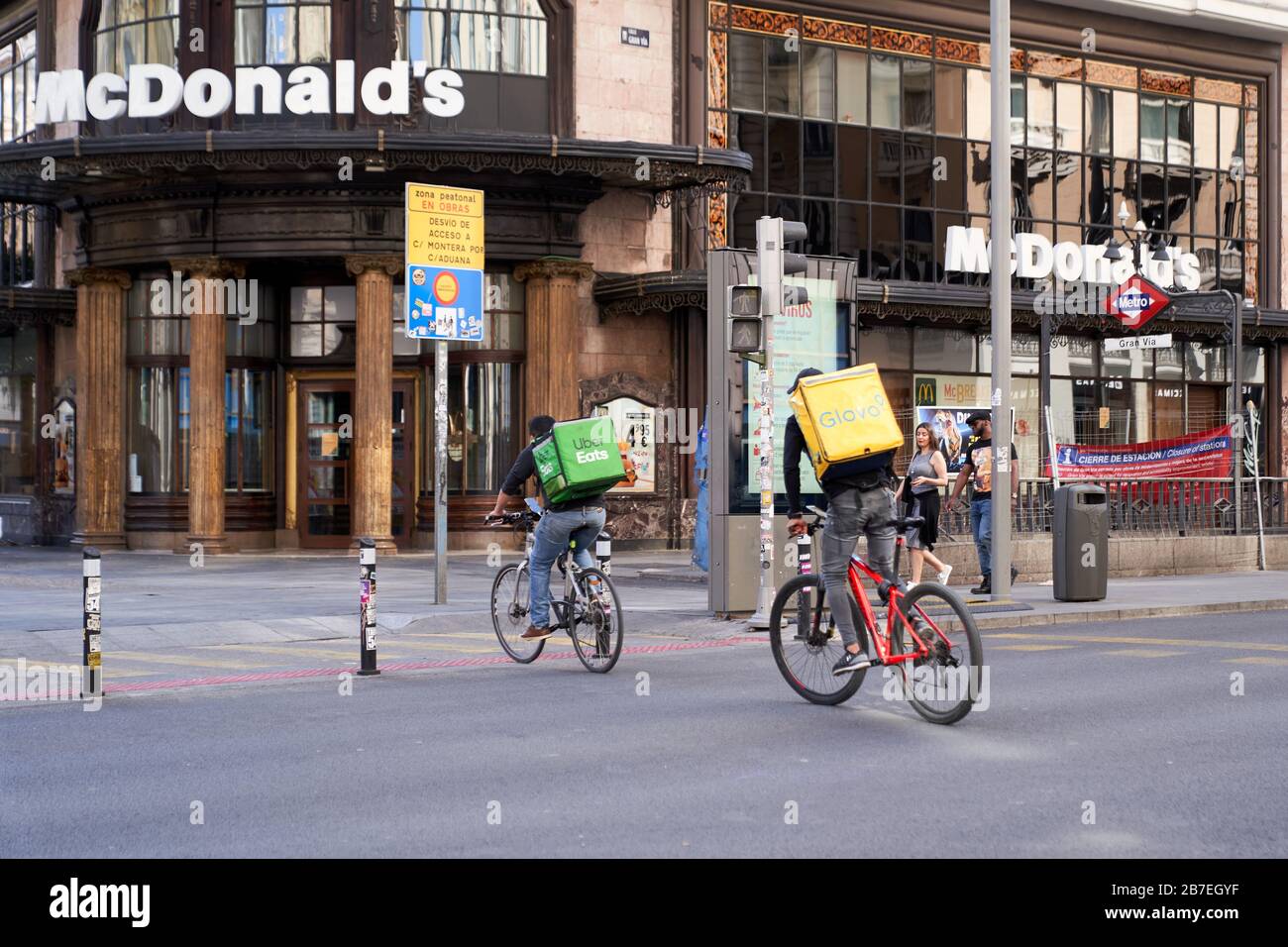 An Uber eats and a glovo delivery cyclist ride across Gran Via, Madrid, passing the few pedestrians during the State of Emergency for Corona virus Stock Photo