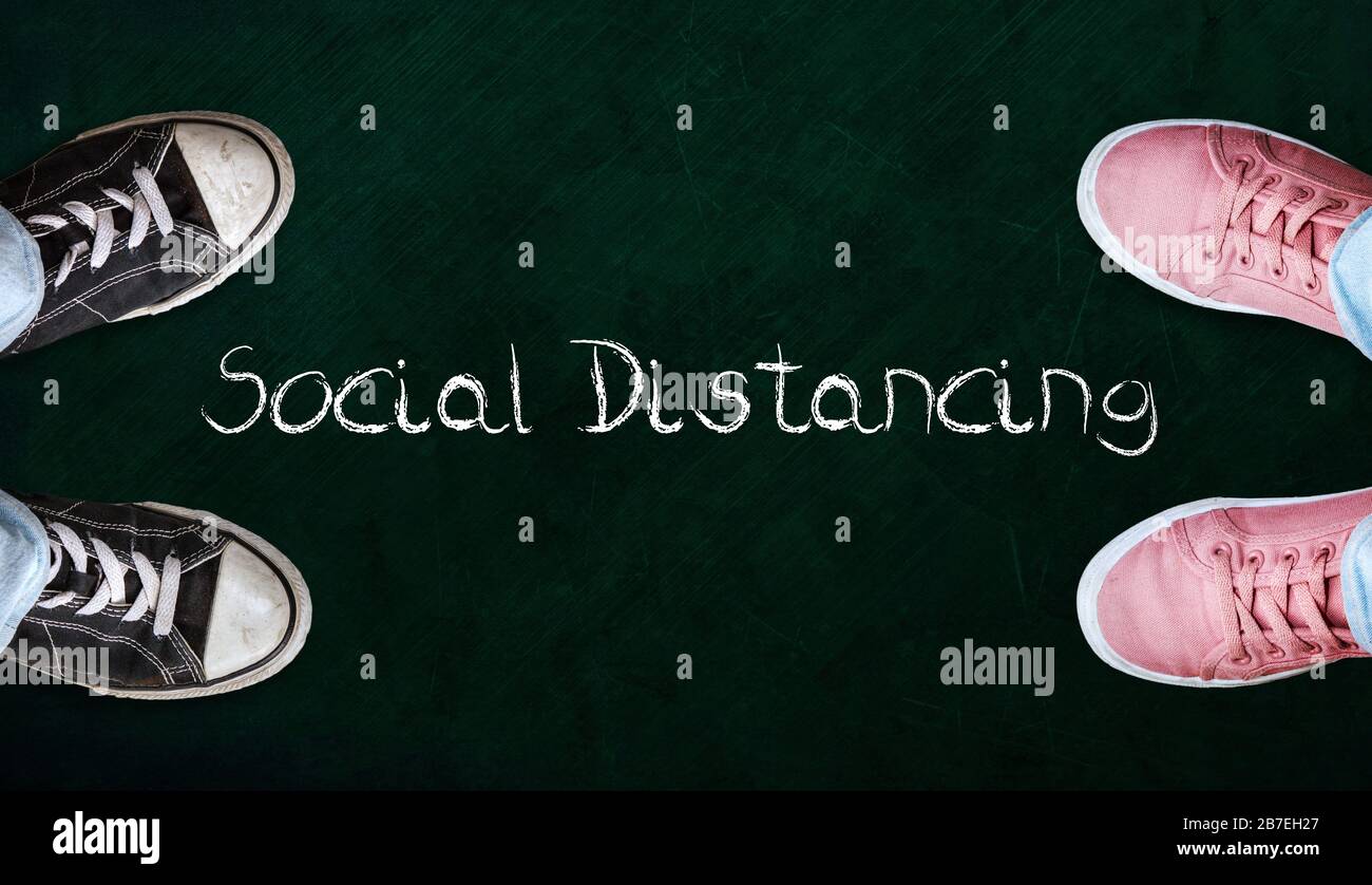 Two people standing on chalkboard with the word social distancing in between. Concept of staying physically apart for infection control intended to st Stock Photo