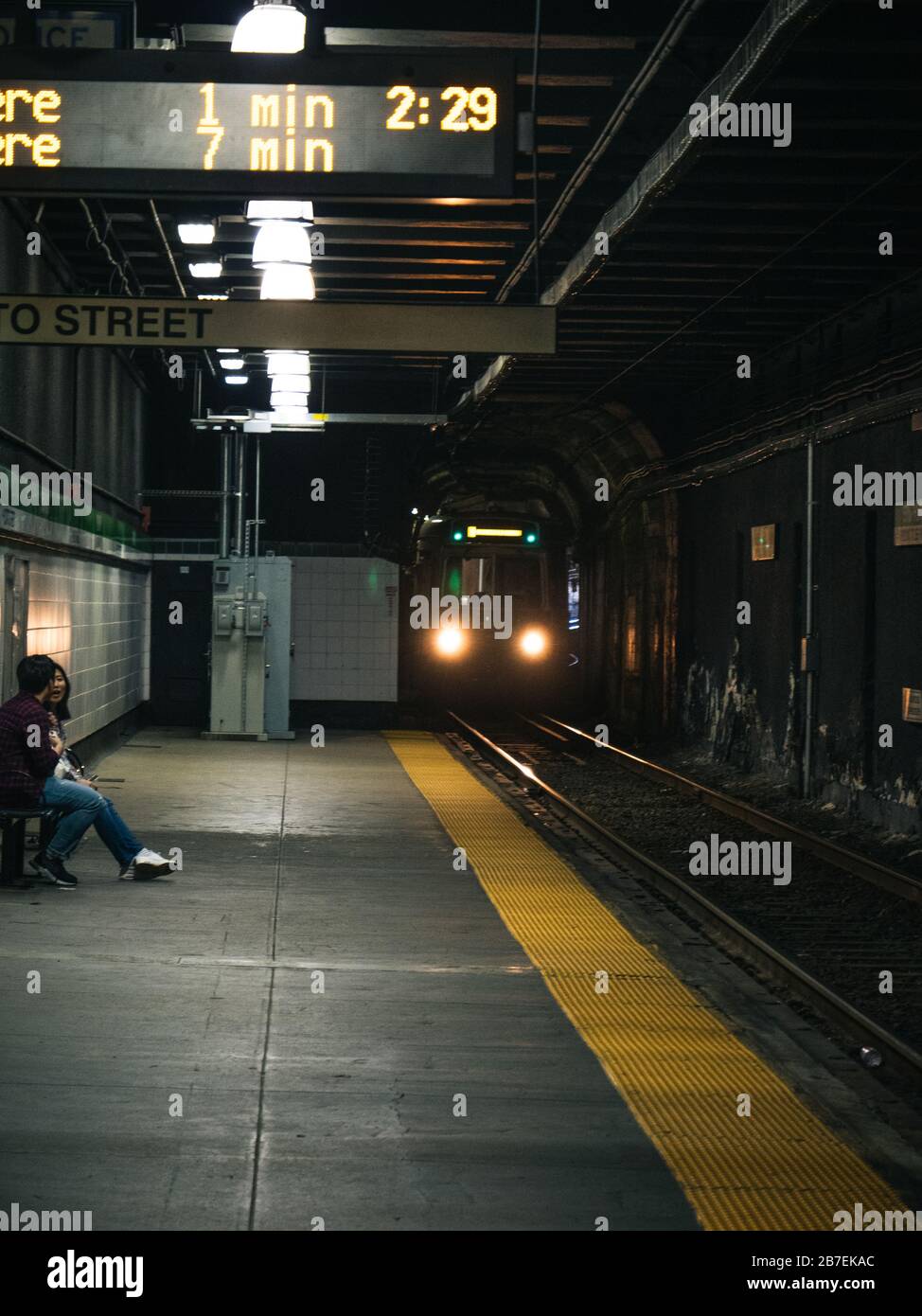 Man and a woman sitting and talking on a bench in a subway with upcoming train Stock Photo