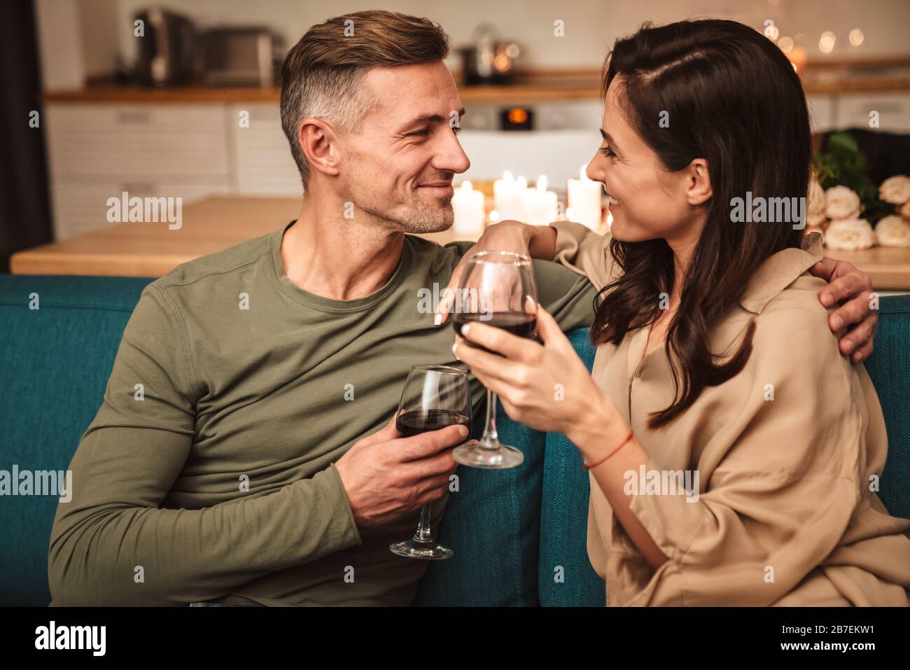 Image of happy passionate couple drinking red wine from glasses while ...