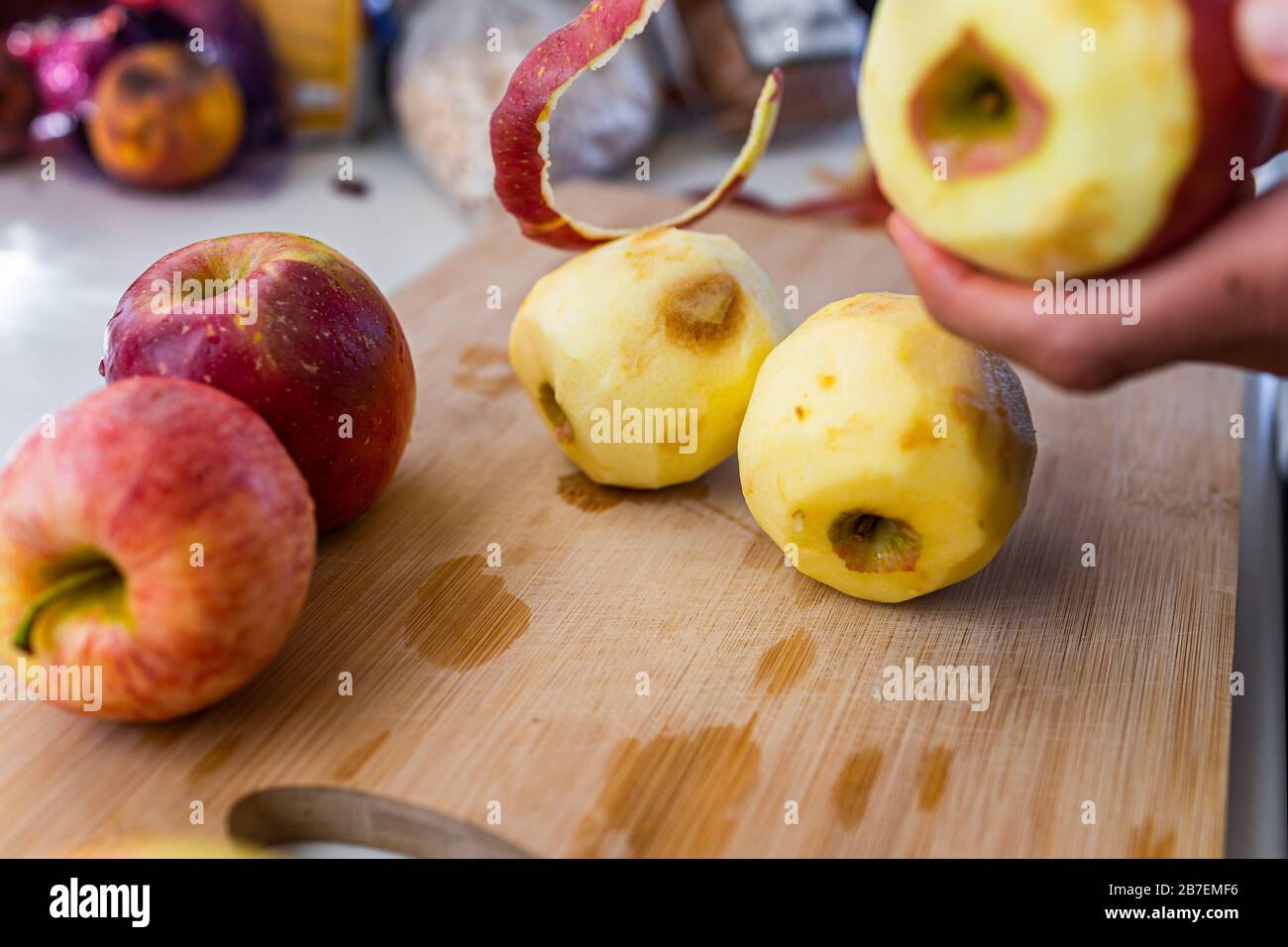 Closeup of wooden cutting board and person hands peeling old red apples