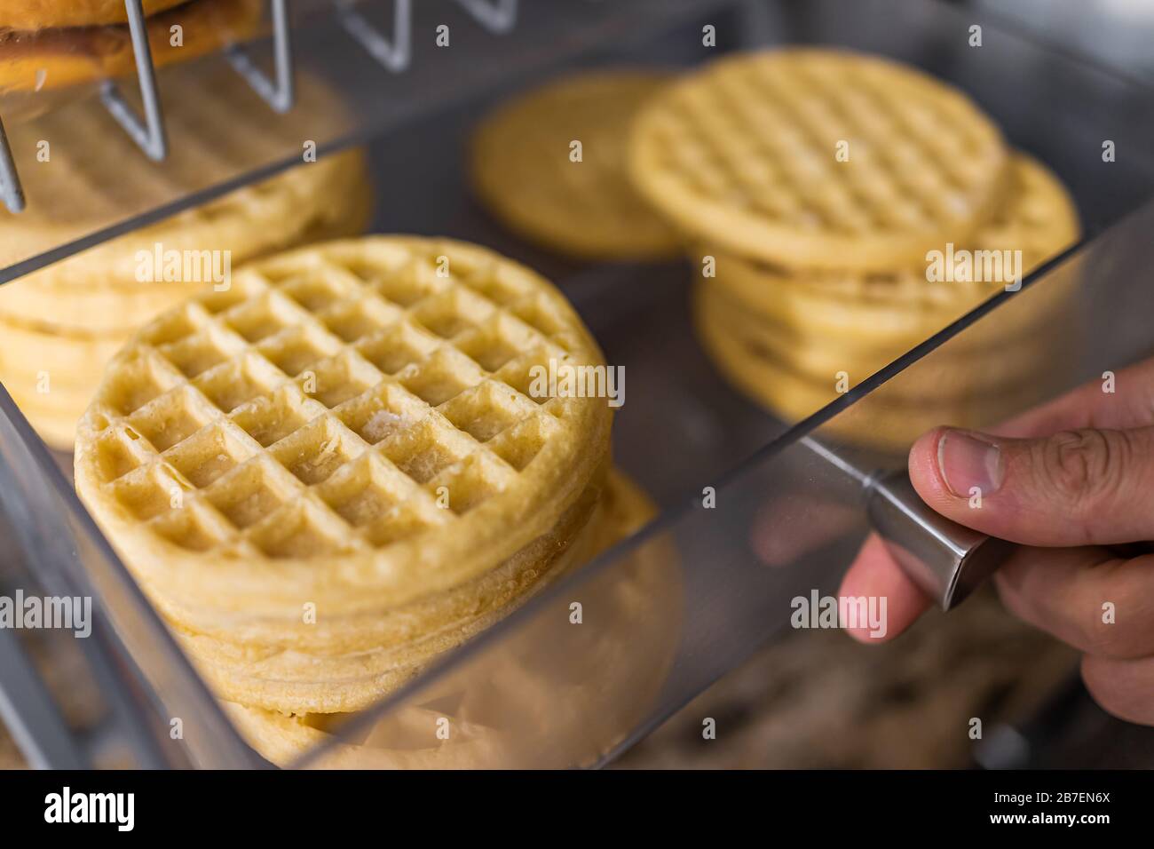 Closeup macro of hand opening waffles on bakery tray buffet for morning continental breakfast in hotel motel or office Stock Photo