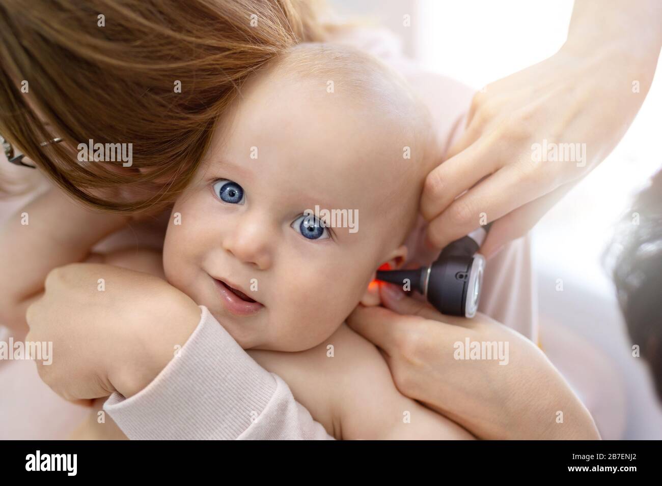 Doctor pediatrist examining childs ear with otoscope. Mom holding baby with hands. Medicine, healthcare ,pediatry and people. Children healthcare and Stock Photo