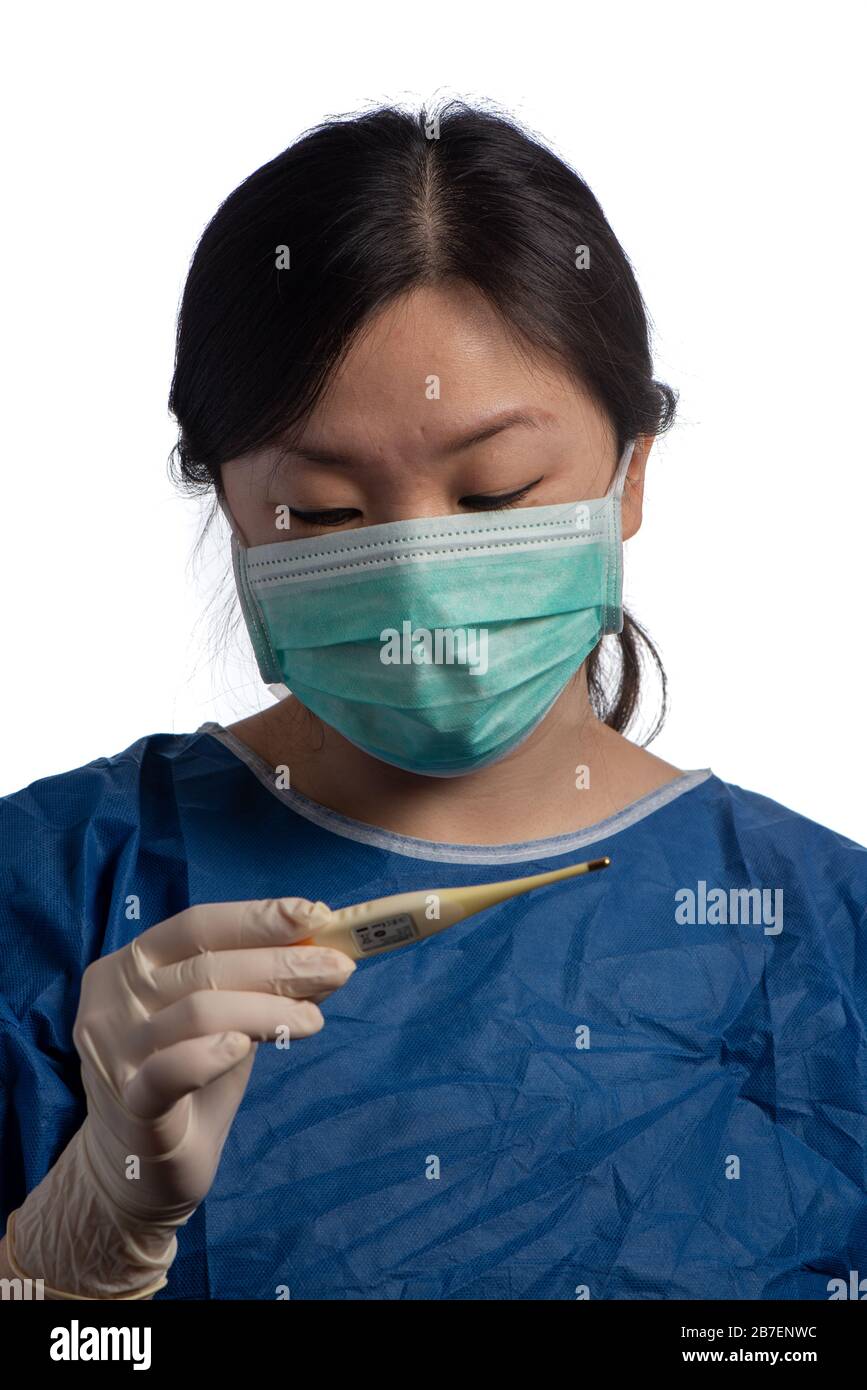 young asiatic physician woman wearing a green protection mask with medical gloves reading a thermometer reading temperature on a white background Stock Photo